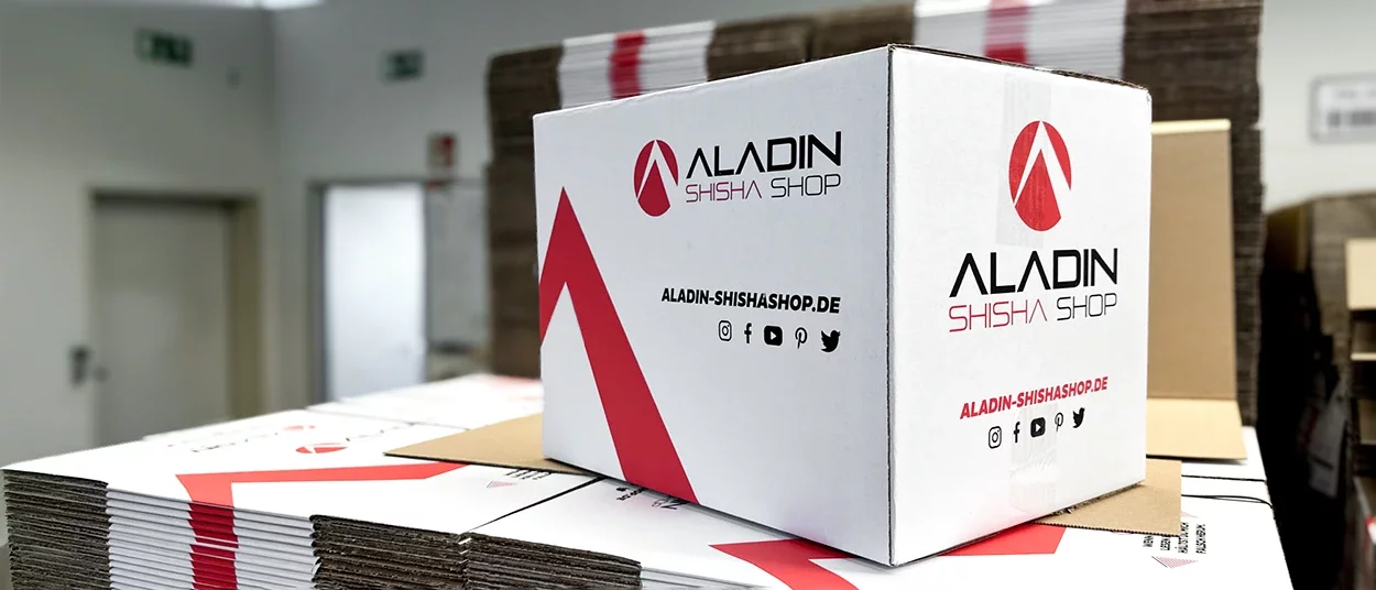Weißer Karton mit Aladin Shisha Shop Logo auf einem Stapel zusammengefalteter Kartons